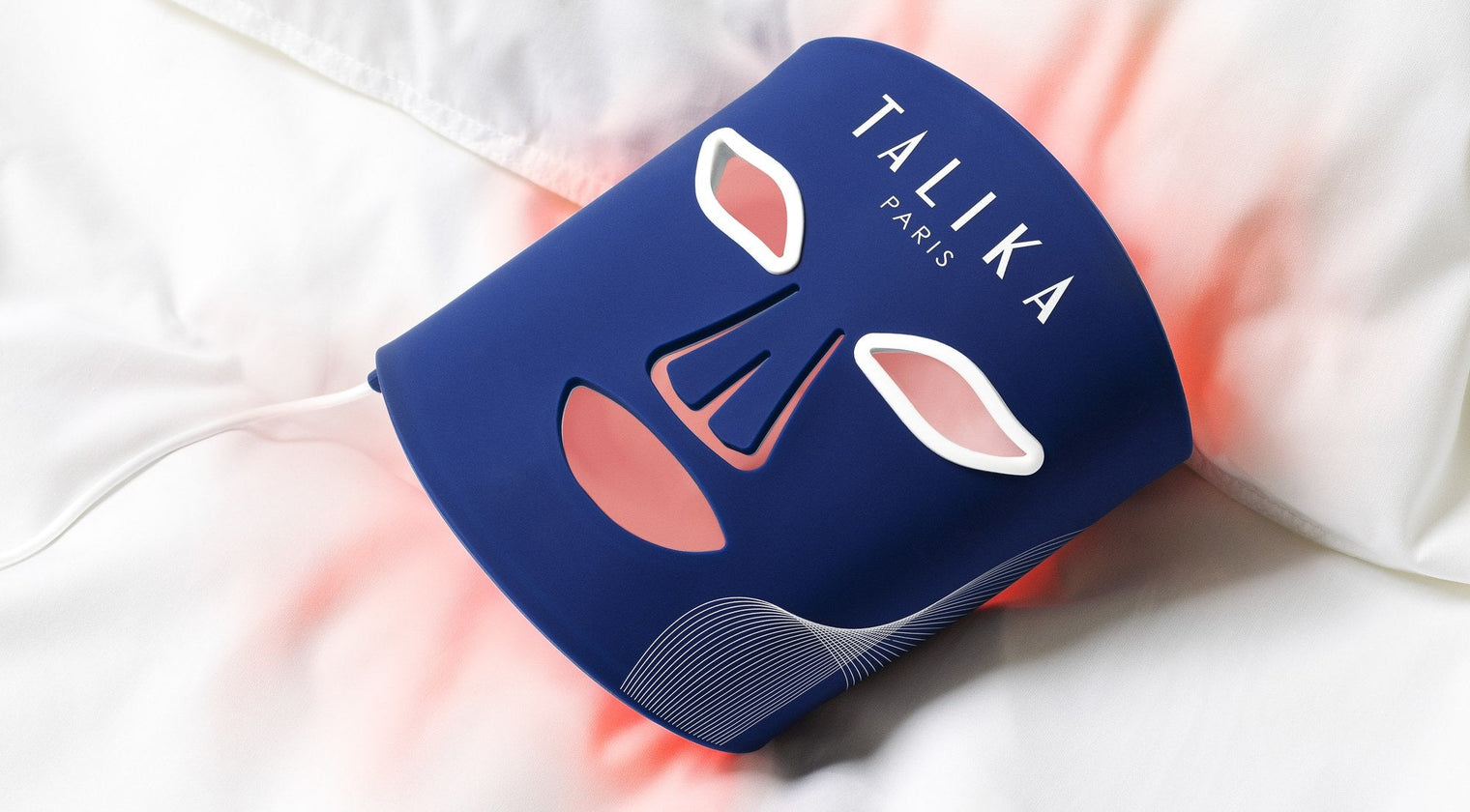 Le LED Therapy Mask de Talika allumé en rouge, posé sur un drap blanc